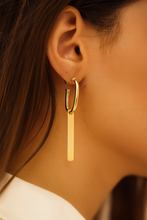 Load image into Gallery viewer, Gold hoop earring with a dangling bar worn by a person