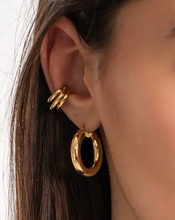Load image into Gallery viewer, Close-up of a person wearing gold hoop earrings with a blurred background
