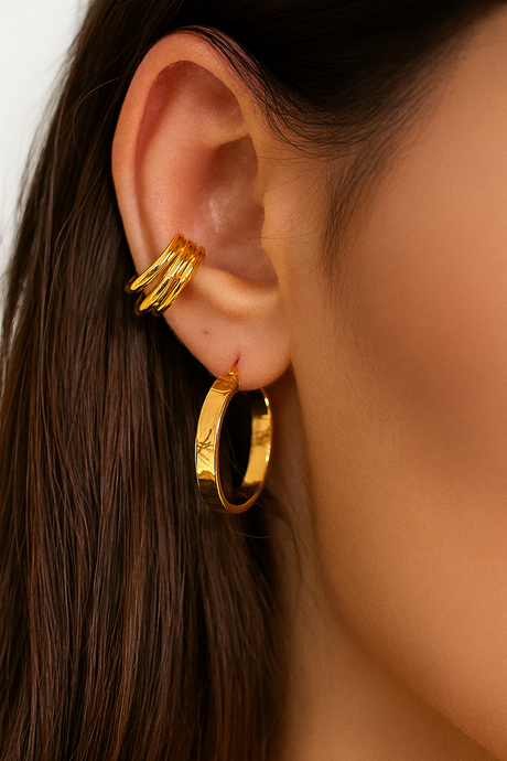 Close-up of a person wearing gold hoop earrings with a plain background