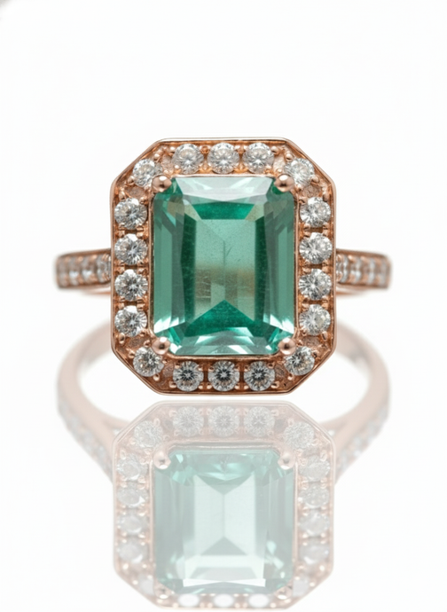 Ring with emerald green gemstone and rose gold setting on a white background