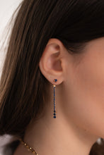 Load image into Gallery viewer, A person wearing a gold-colored earring with a blue charm and a chain design.
