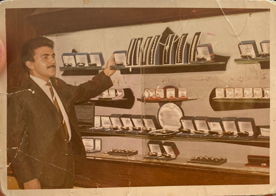 Vintage photograph of a man in a suit standing in front of a display case with various items.