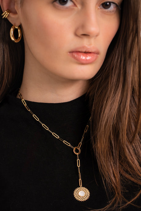 A person wearing a black tank top adorned with a gold-colored chain necklace featuring a circular charm pendant.