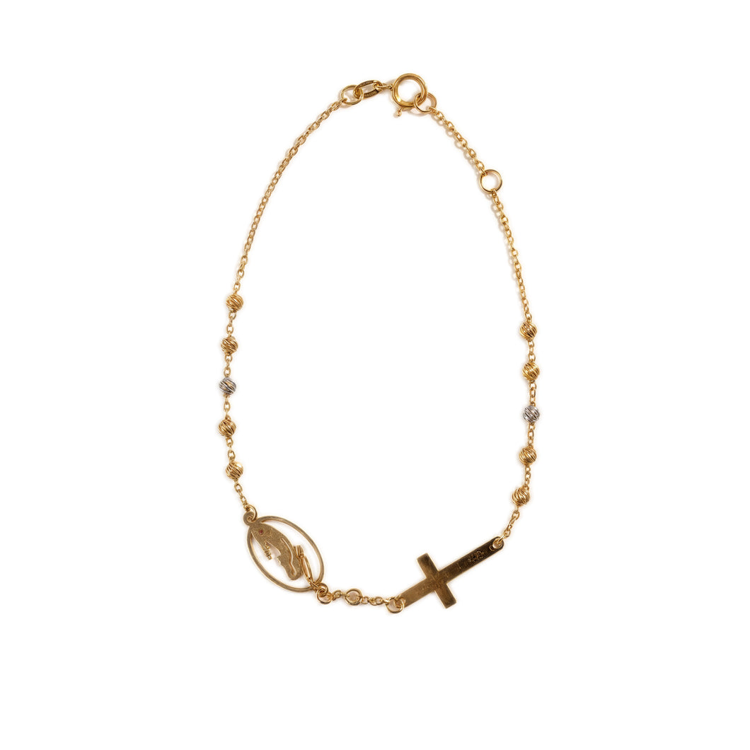 A gold-colored necklace with a chain link design, featuring a charm in the shape of a cross and a circular charm that may represent a dreamcatcher or a similar symbol.